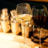 木のテーブルに並ぶ白ワインと赤ワインのグラスの写真