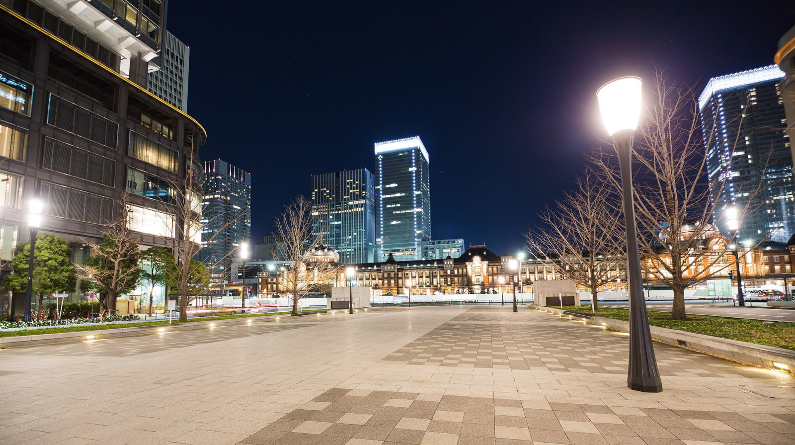 石畳の広場に街灯と樹木が並び奥に高層ビルが見える夜の東京駅前