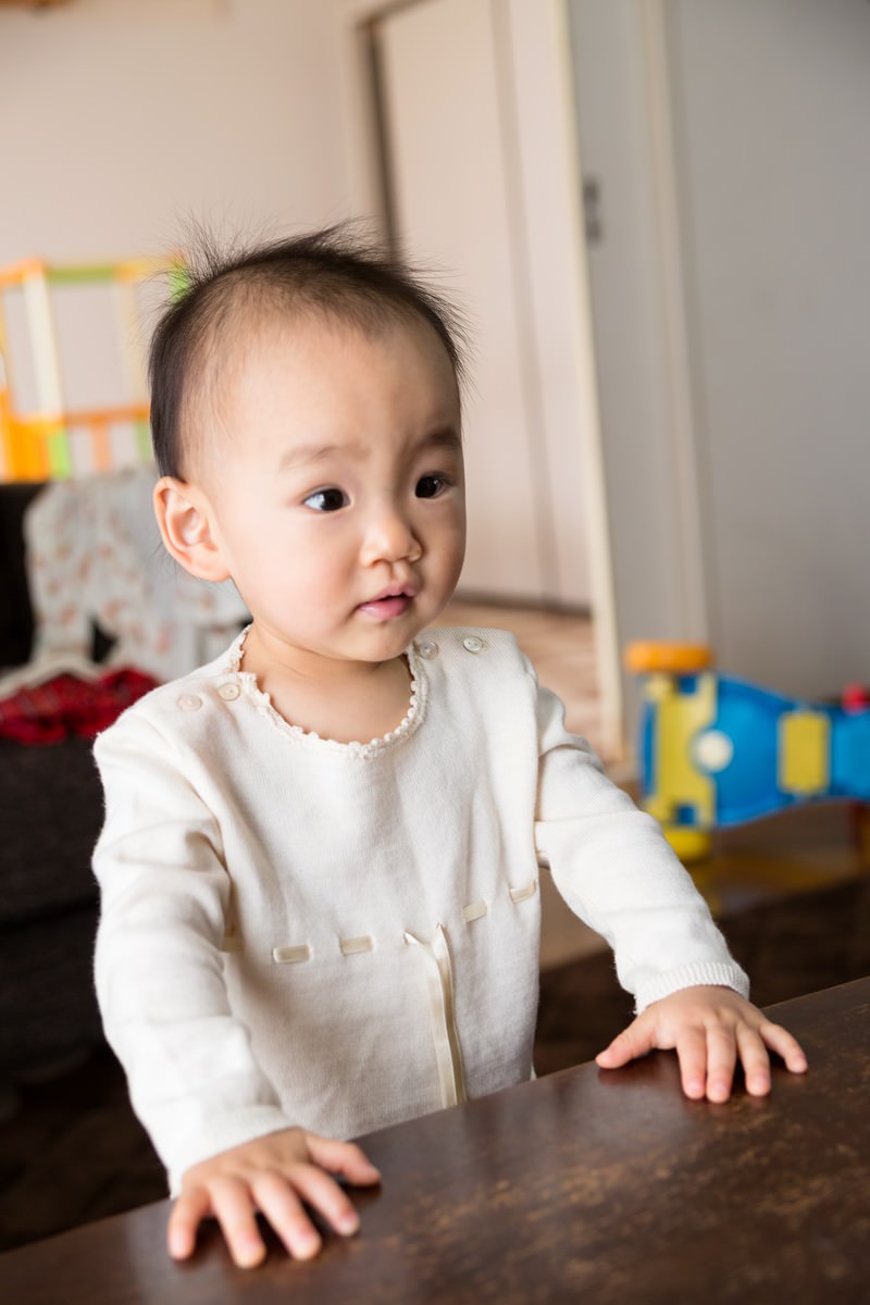 テーブルにつかまり立ちして何かを見る赤ちゃん［モデル：あんじゅ］