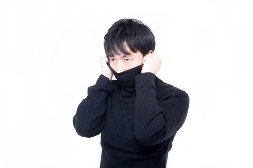 黒いタートルネックの襟を両手で引き上げる男性の正面ポーズ