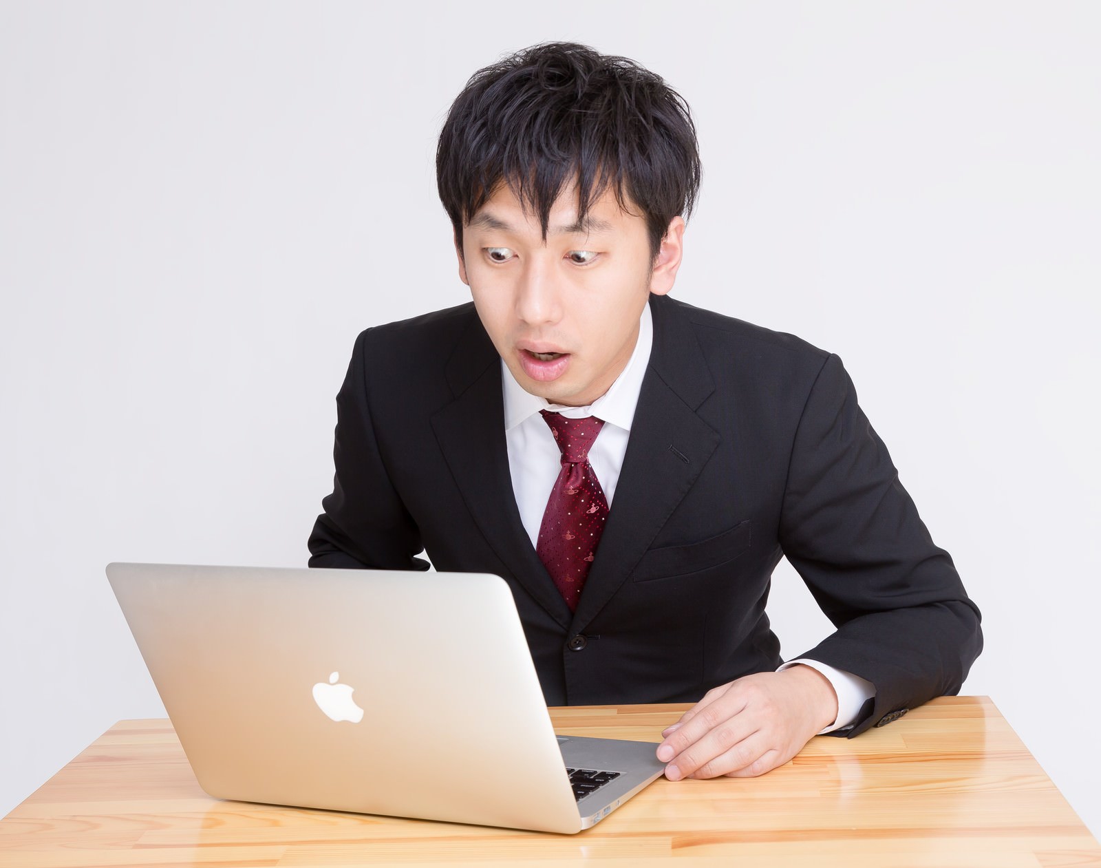黒いスーツの男性がノートパソコンを見て口を開けて驚いた表情をしている［モデル：大川竜弥］