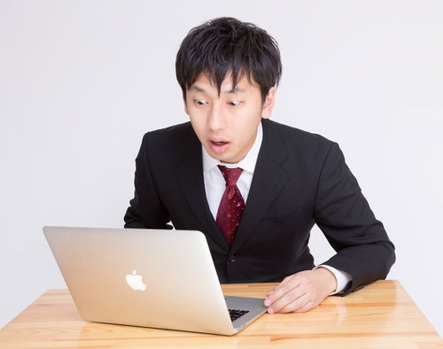 PCを見て「ヤバいことになった」っと驚く表情のビジネスマン