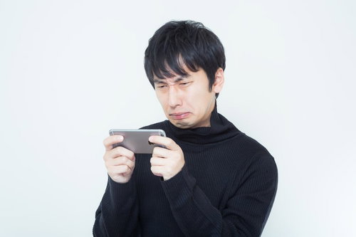 黒いタートルネックでスマホを横向きに持って見る男性