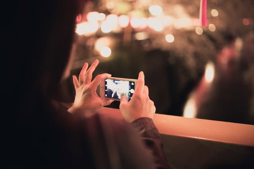 ぼけた暖色系の光の中でスマホを両手で持って撮影する手元の接写