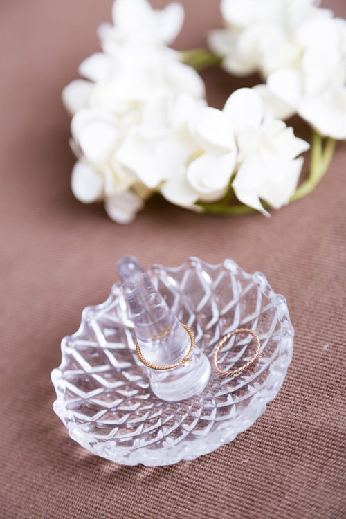 ガラス皿に置かれた金色の結婚指輪と白い花