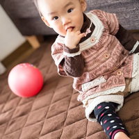 指を咥えて布団の上に座る赤ちゃんの写真