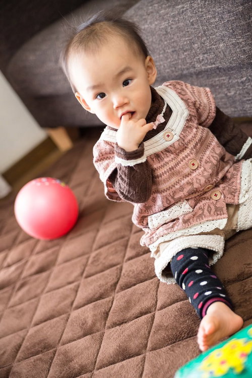 指を咥えて布団の上に座る赤ちゃん