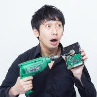 ドリルとHDDを持って焦った表情で目を見開く黒シャツの男性の写真