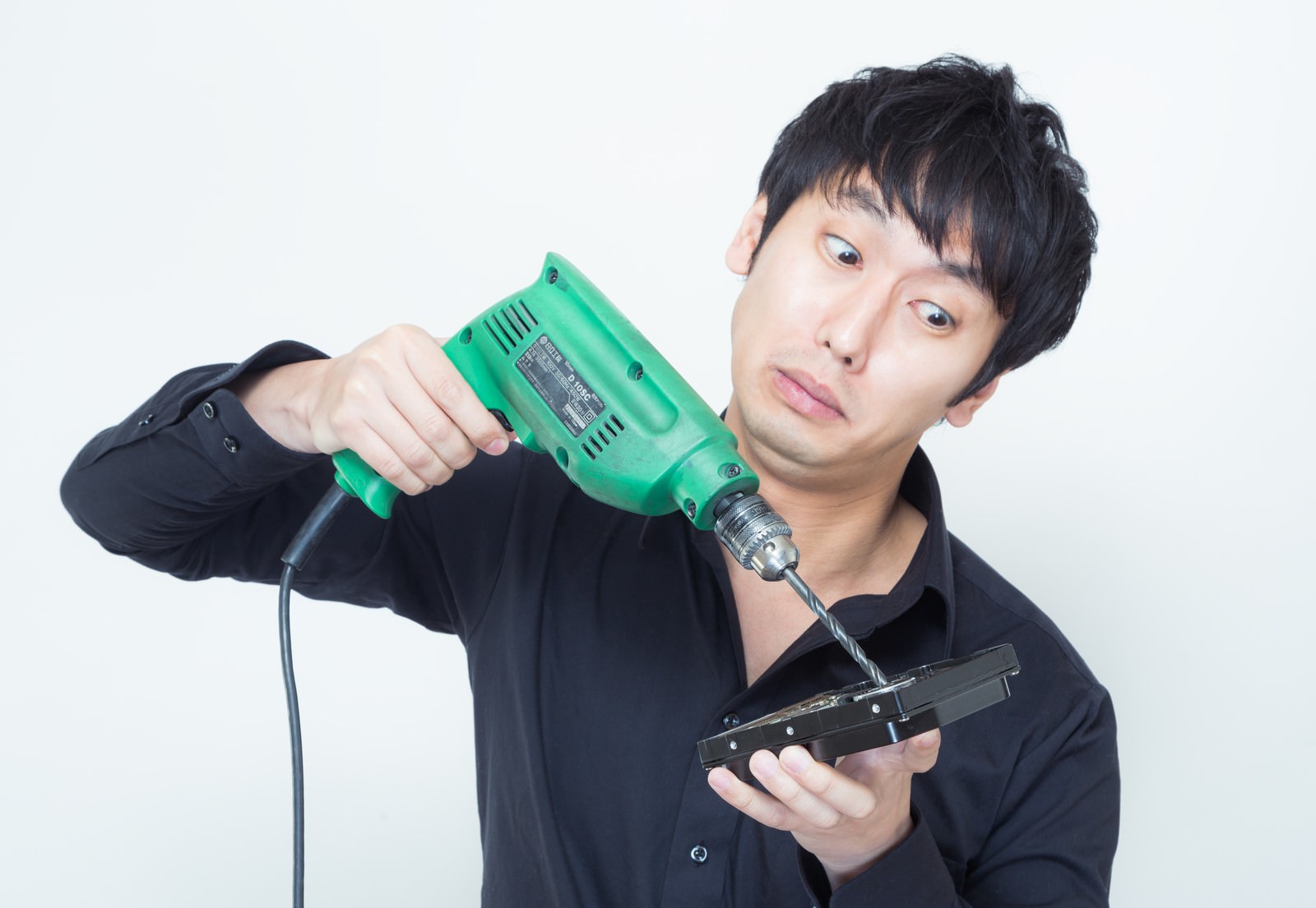 ハードディスクに電動ドリルを向ける男性［モデル：大川竜弥］