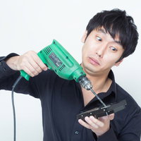 ハードディスクに電動ドリルの先端を向ける黒い服の男性の写真