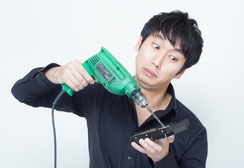 ハードディスクに電動ドリルの先端を向ける黒い服の男性