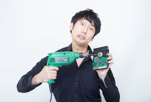 電動ドリルとハードディスクを持って目を見開く黒シャツの男性