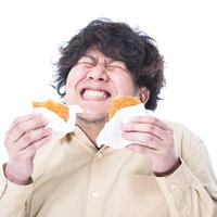 両手に揚げたてのコロッケを持って笑顔の男性の写真