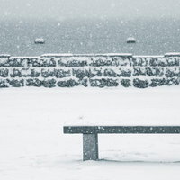 雪が降る中で石垣の塀の前に置かれた雪が積もった木製ベンチの写真