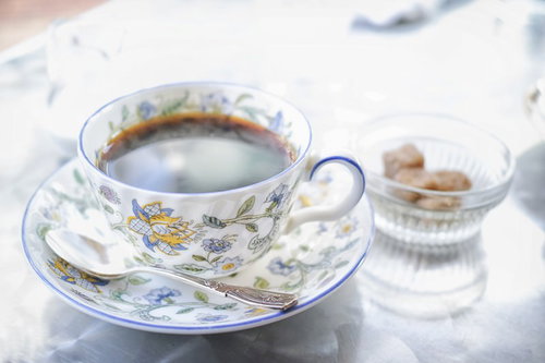 花柄のティーカップに入った紅茶と角砂糖のガラス容器