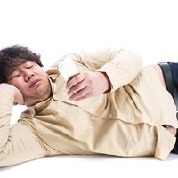 横たわってスマートフォンを操作する太った男性の写真