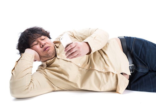 横たわってスマートフォンを操作する太った男性