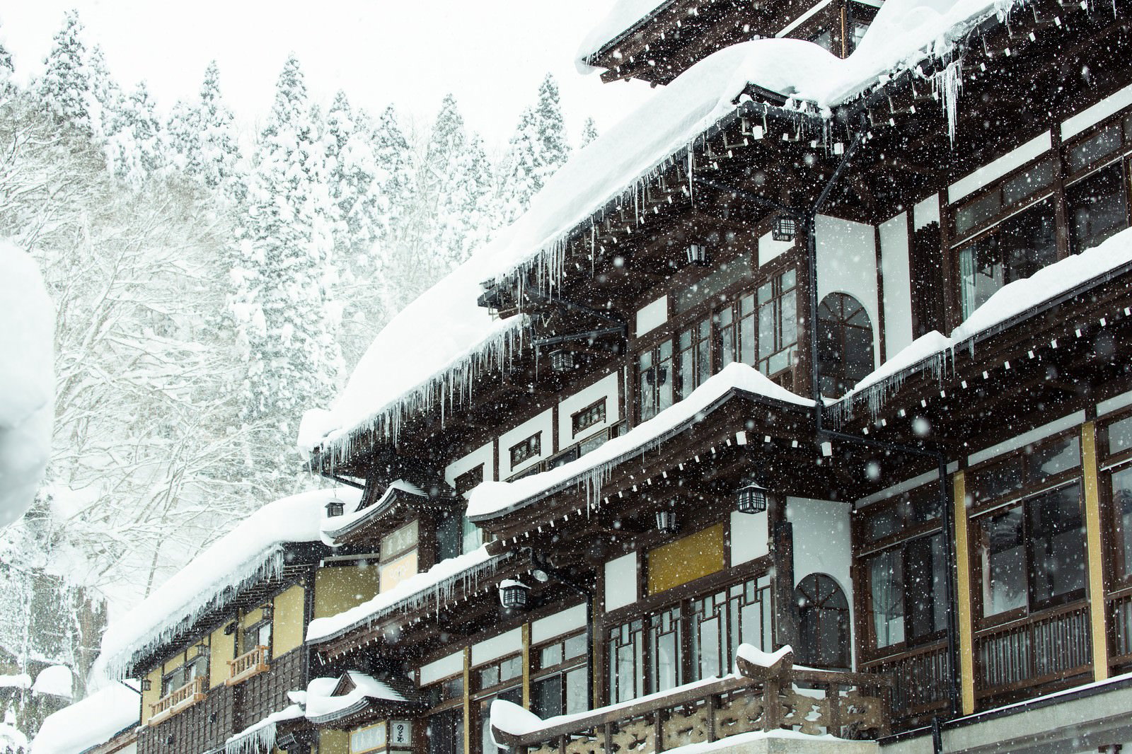 屋根につららが垂れ下がる雪に覆われた銀山温泉宿の木造建物
