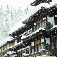 屋根につららが垂れ下がる雪に覆われた銀山温泉宿の木造建物の写真