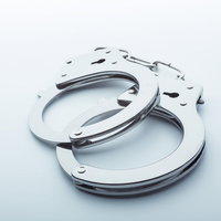 白い面の上に開いた状態で置かれた鎖付きの金属製手錠の写真