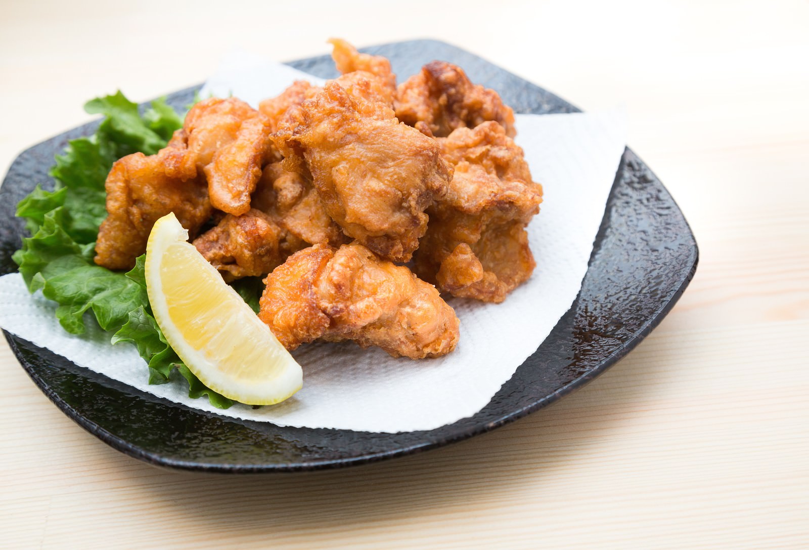 木の机の黒い丸皿にレタスとレモンを添えた唐揚げ