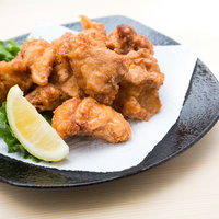木の机の黒い丸皿にレタスとレモンを添えた唐揚げの写真