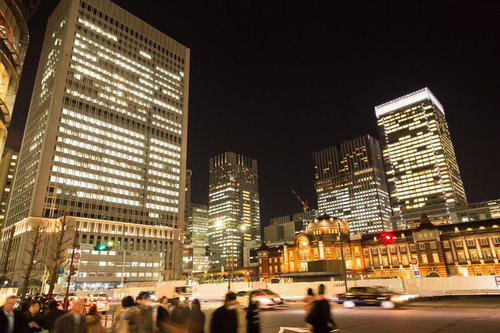 レンガ色の東京駅と高層ビルの明かりが映える夜の道路風景