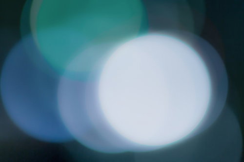 暗い場所に浮かぶ白や青のぼやけた丸い光のボケ写真