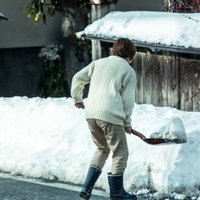 雪が積もった屋外でシャベルを使って雪かきする人の写真