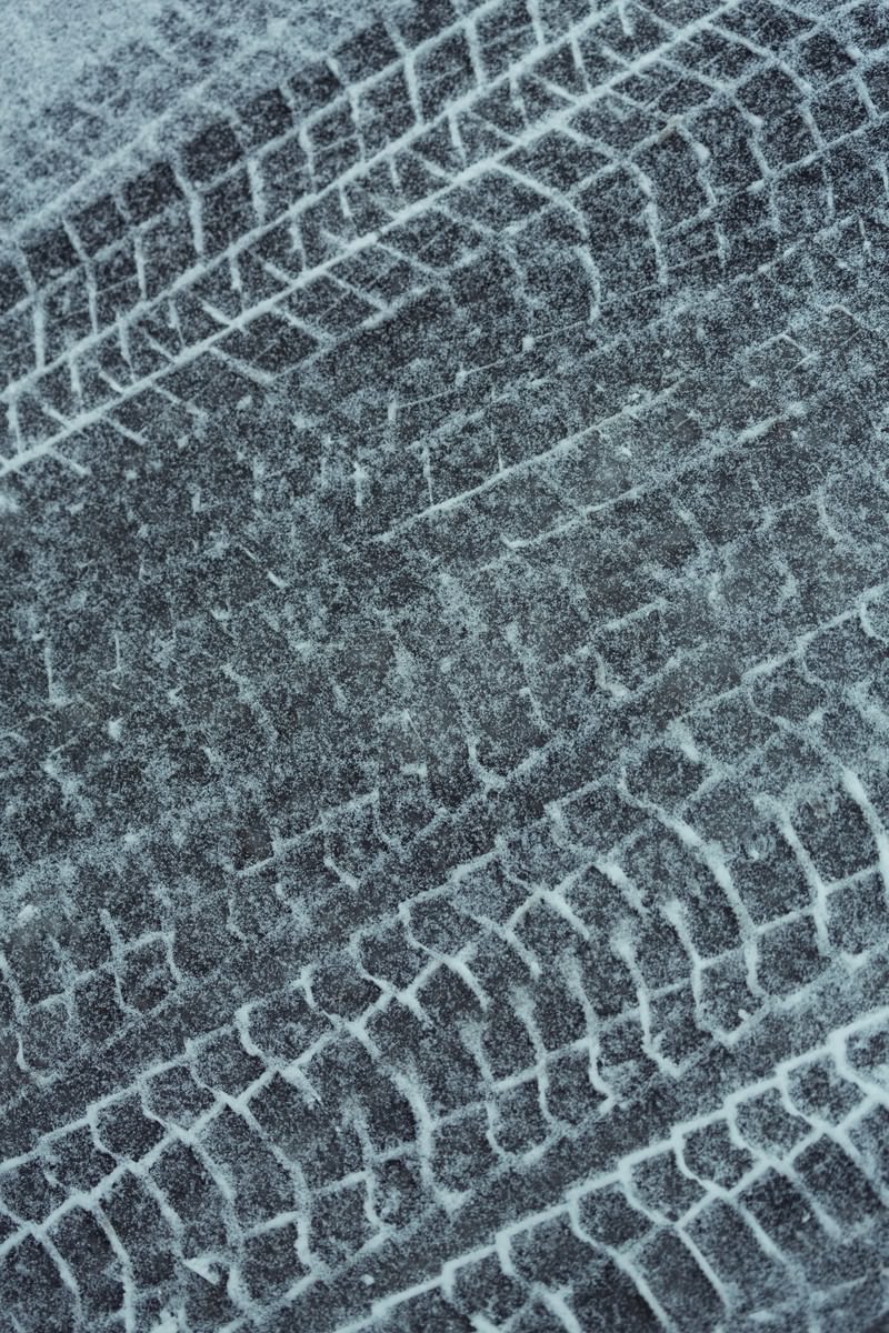 暗い地面に白いタイヤ跡が残る雪のアスファルトのテクスチャー