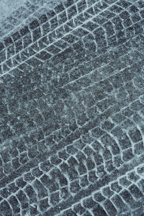 暗い地面に白いタイヤ跡が残る雪のアスファルトのテクスチャー