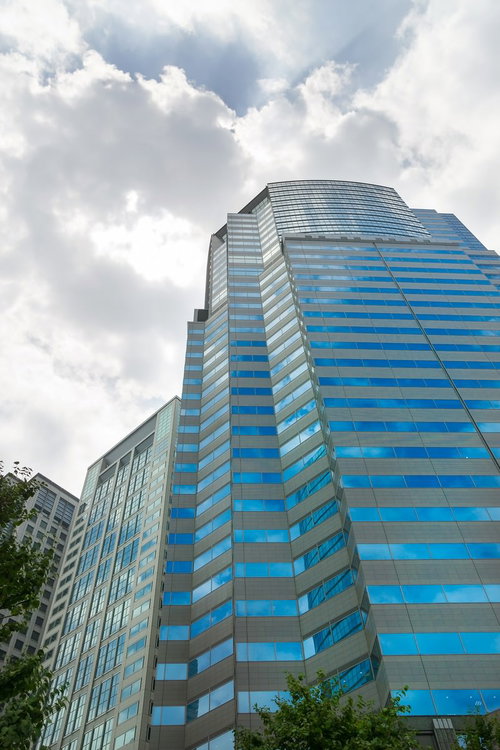 青いガラス窓が並ぶ高層ビルと白い雲