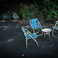 アスファルトの上の折りたたみ椅子と丸テーブルの朽ちた休憩場所の写真