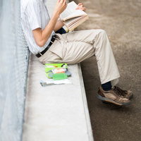 コンクリートに座って本を読む男性の写真