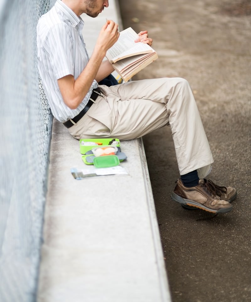 コンクリートの段差に座り本を読む男性