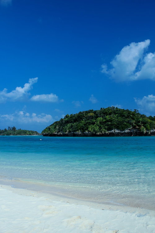 白い砂浜と小さな島が浮かぶ沖縄の青い海