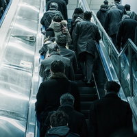 黒や濃い緑のコートを着た人々が上るエスカレーターの出勤風景の写真