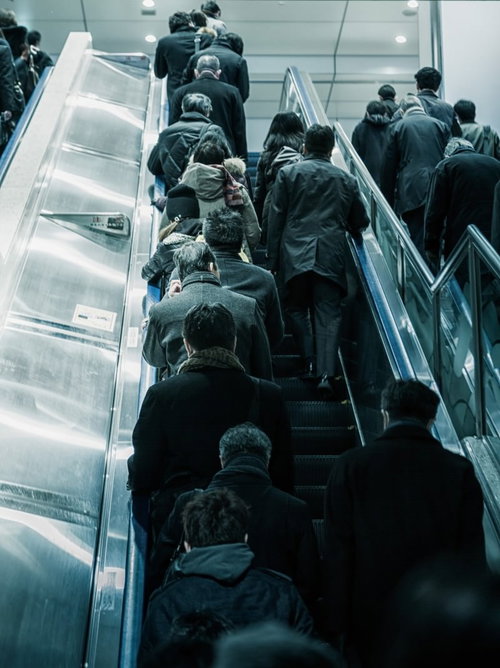 黒や濃い緑のコートを着た人々が上るエスカレーターの出勤風景