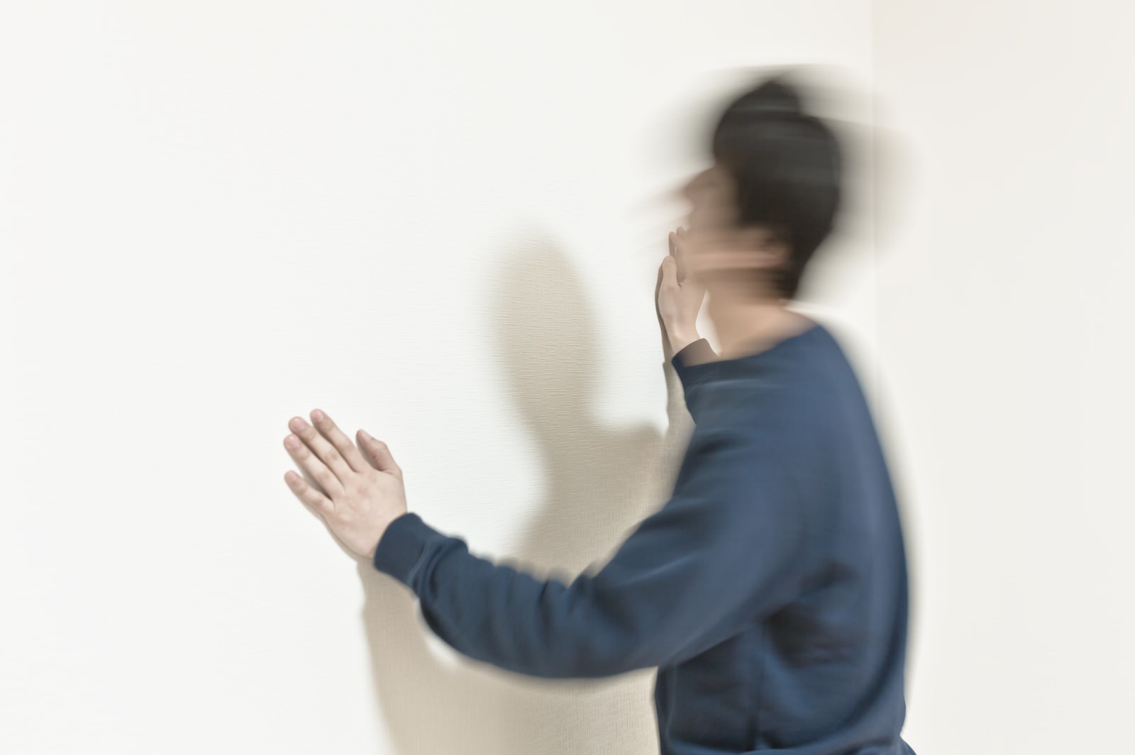 白い壁の前で青い服の人物が頭を振り動きのブレと複数の影が映っている［モデル：大川竜弥］