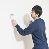 ハンマーで壁を連打するスウェット姿の男性の写真