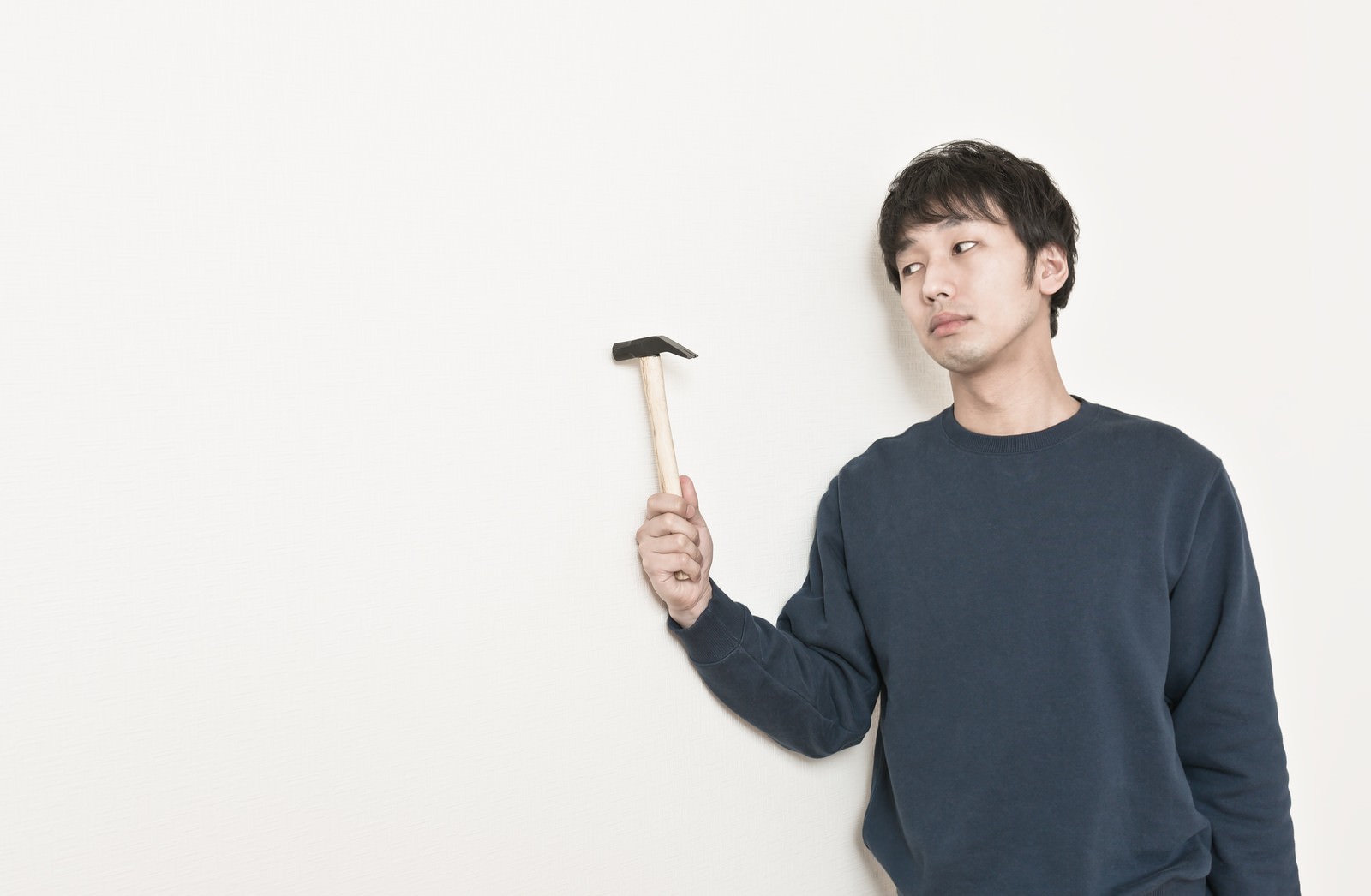 紺色のトレーナーを着た男性が木の柄のハンマーを右手で掲げている［モデル：大川竜弥］