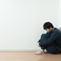 部屋の隅で膝を抱えてうつむく男性の写真