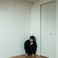 部屋の隅でしゃがみ込む黒い服の男性の写真