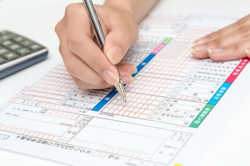 電卓を横に確定申告書にペンで記入する手元