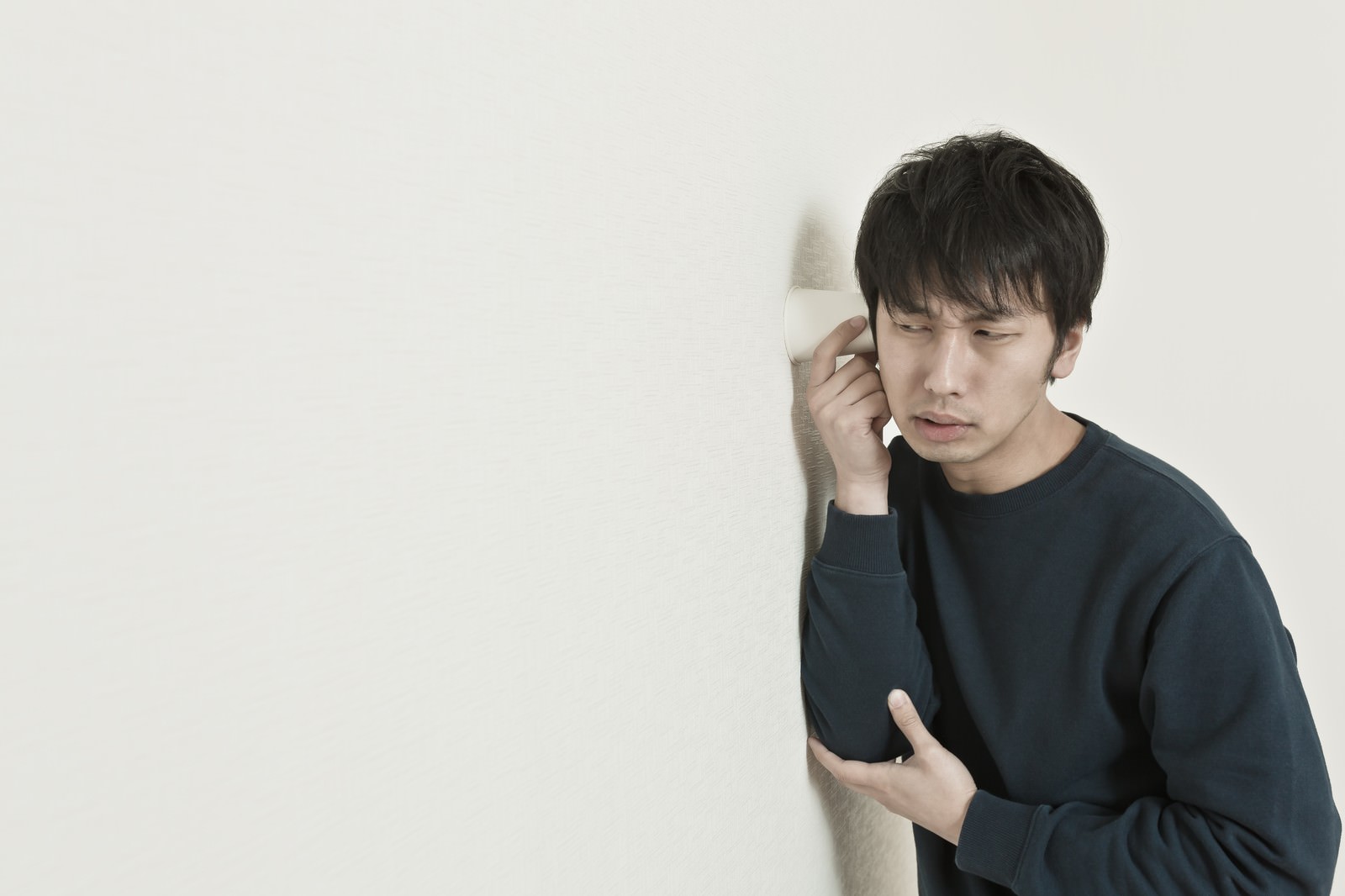 壁に耳を当てて盗み聞きする男性［モデル：大川竜弥］