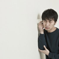 紙コップを耳に当て、隣の会話を盗み聞きする男性の写真