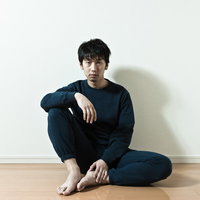 ワンルームの床に座るスウェット姿の男性の写真