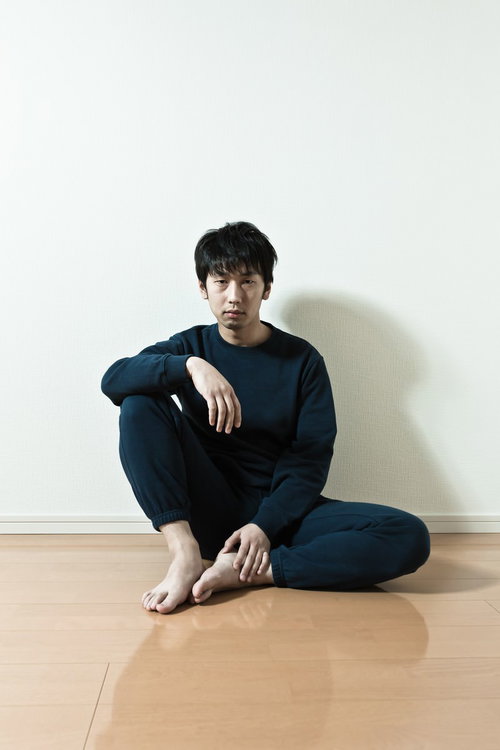 ワンルームの床に座るスウェット姿の男性