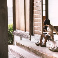 レンガ壁の建物の段差に腰かける子供の後ろ姿の写真