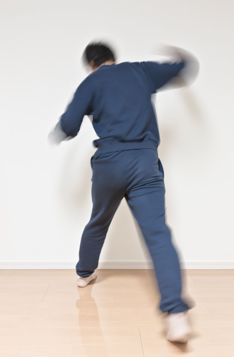 白い壁の前で紺色の上下の人物が後ろ向きに両腕を広げ動きでブレている［モデル：大川竜弥］